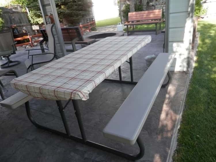 A picnic table lined with a fitted sheet to prevent the sheet from being blown away by the wind.