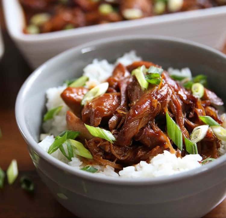 bowl of honey bourbon chicken over white sticky rice with and topped with diagonally sliced green onions or sifflets 