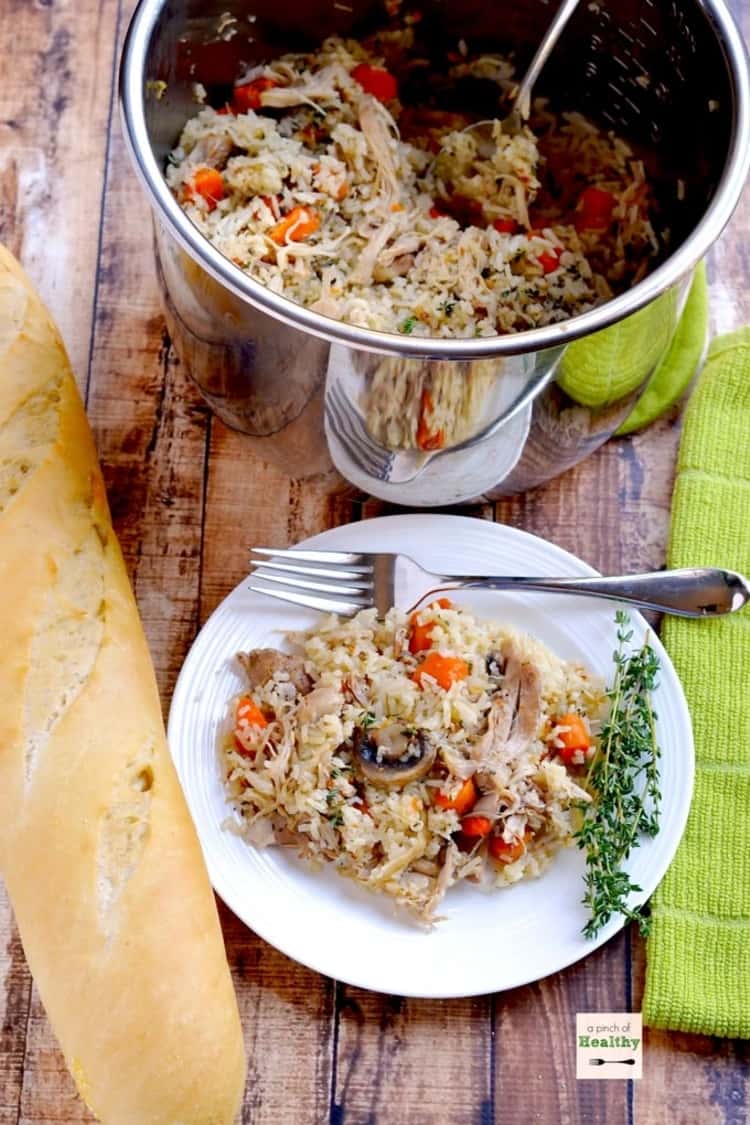 Plate of chicken and rice served on a plate with sprig of rosemary and a fresh loaf of french bread beside it