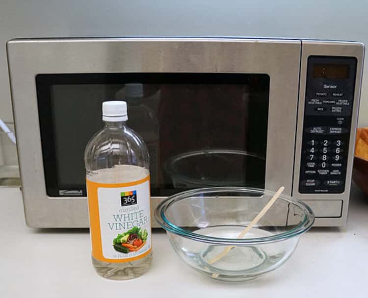 white vinegar, water in a glass bowl, and a wooden pick, in front of a microwave 