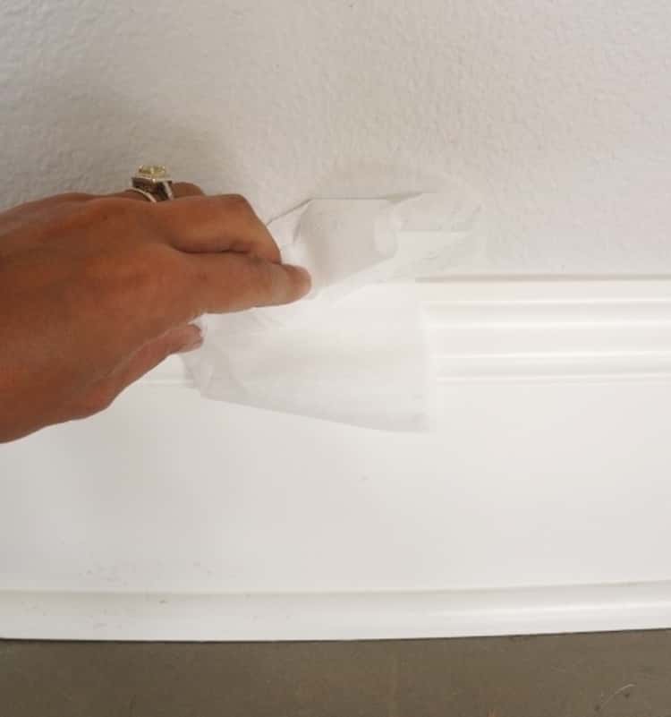 person cleaning the baseboard using a dryer sheet 