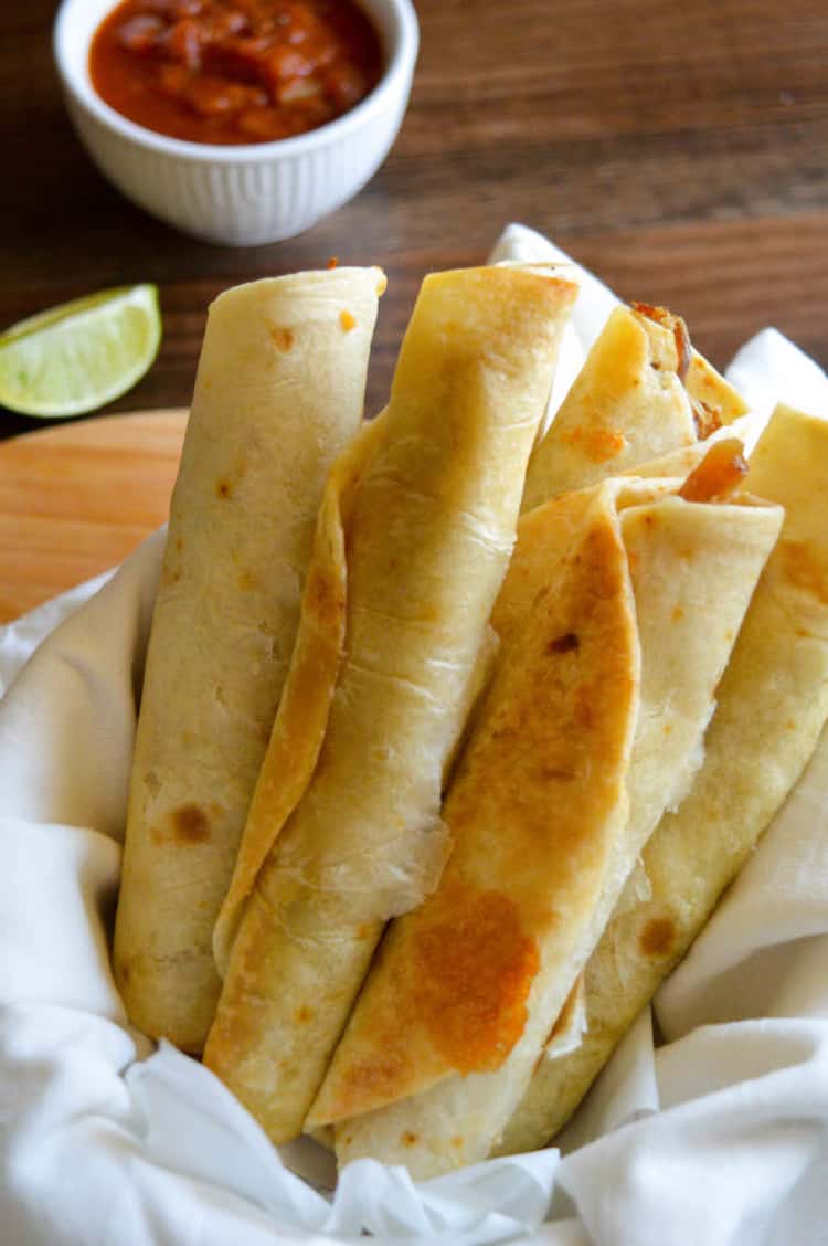 Air-fryer taquito rolls with wedge of lemon and bowl of dipping sauce on the side.
