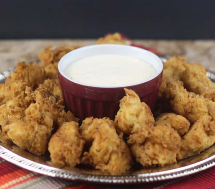 Crispy air fryer chicken nuggets arranged in plate around bowl of white dipping sauce