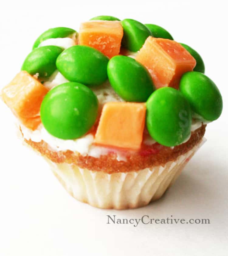 A cupcake topped with peas and carrots which in reality are green skittles and orange toffee 