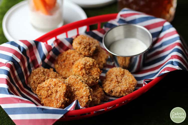 Crispy coated air- fried pickles in red basket with white dipping sauce