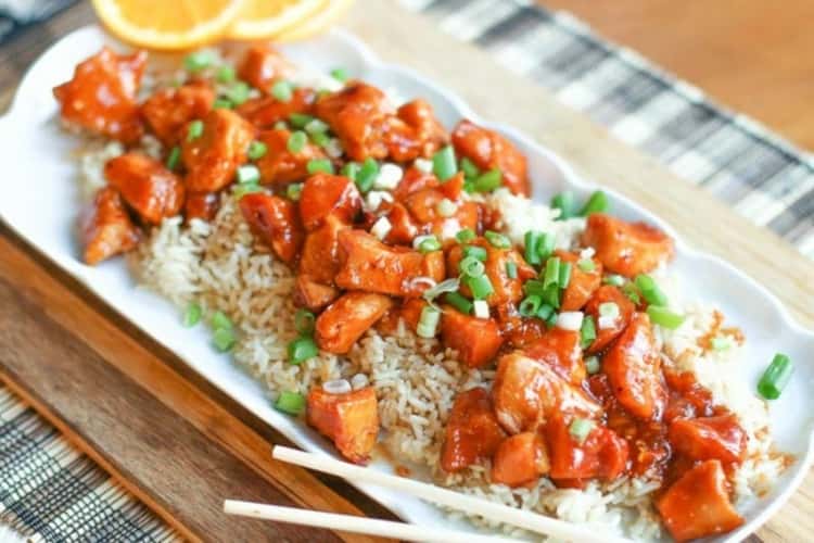 Instant pot  orange chicken over rice served on a large family style platter with orange wedges and chopsticks 