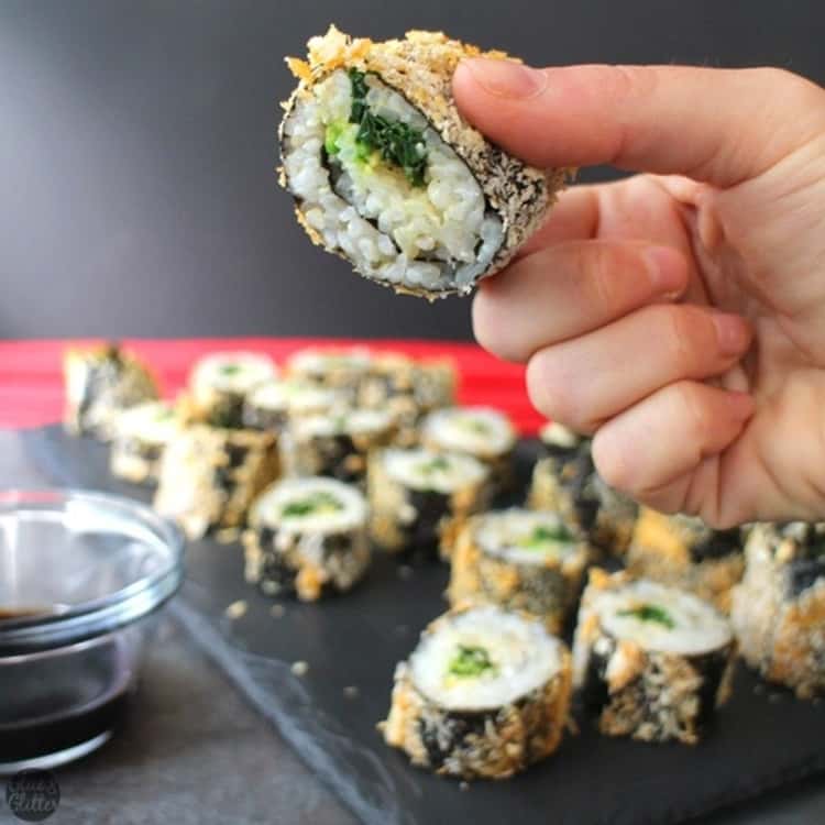 Hand holding a small sushi roll; air fryer sushi rolls arranged on board.