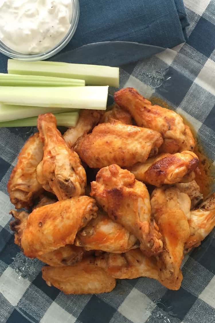 Air-fried buffalo chicken wings in glass plate with celery and dipping sauce on the side.
