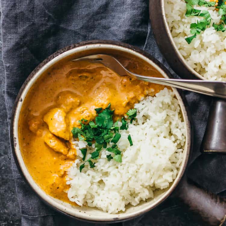 bowl of white rice and chicken tikka masala topped with cilantro