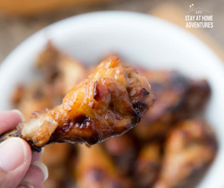 hand holding sweet and sour chicken wing with a bowl of chicken wings in the background