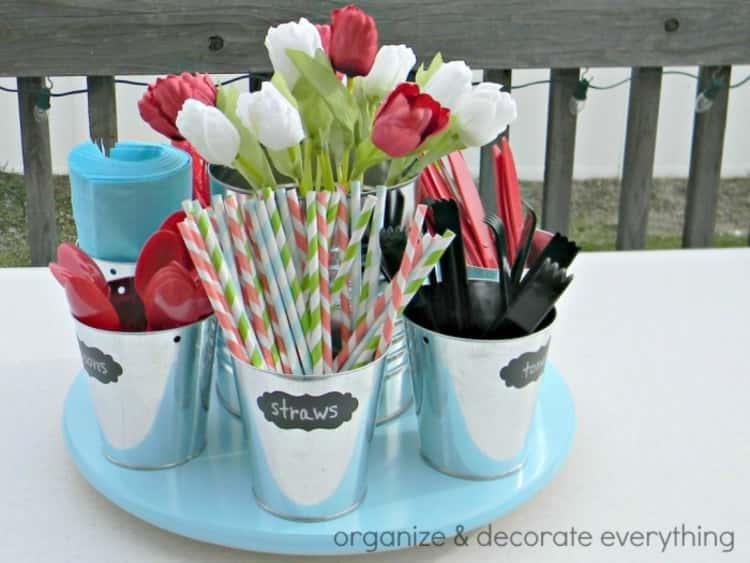 picnic hack - a picnic caddy made from small tins labeled with chalk paper, a larger center pail containing flowers, and a Lazy Susan