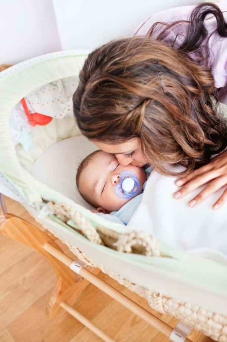 a mom kissing a baby who's asleep and has a pacifier in their mouth