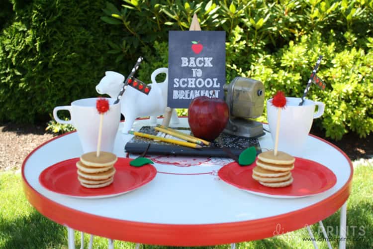 a back-to-school breakfast table set for 2 consisting of some pancakes, apples and complete with a chalkboard sign reading BACK TO SCHOOL BREAKFAST