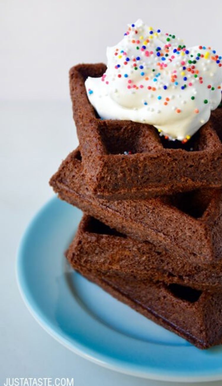 a stack of brownie waffles on a plate with a dollop of vanilla ice cream and rainbow sprinkles