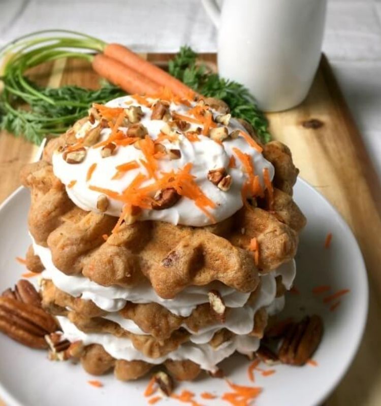 a stack of carrot cake waffles on a plate with cream frosting in between them sitting on top of a cutting board with a beverage mug on the side