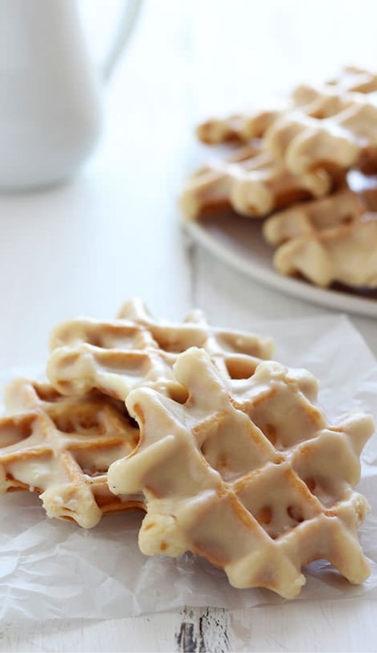 a pile of doughnut waffles with a maple glaze and a plate with more in the background