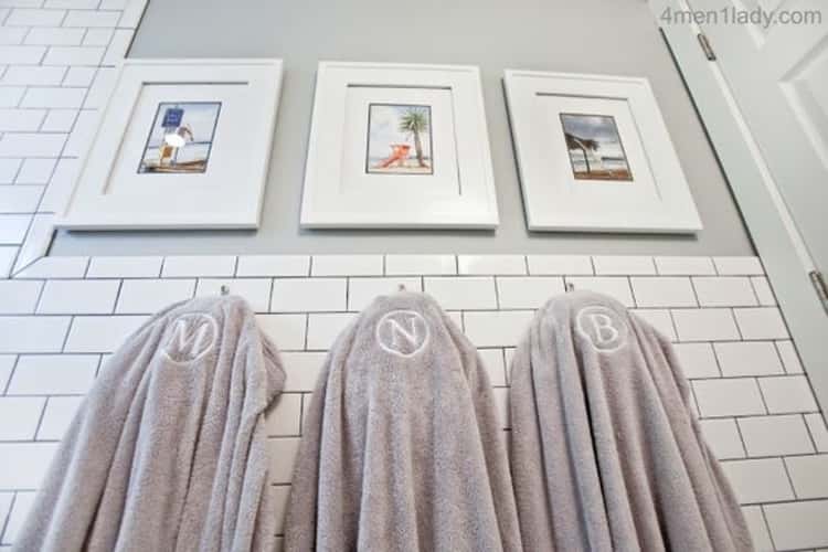 3 hooks on bathroom wall with monogrammed bath towels hanging from them. 3 pictures hanging above the hooks covering the medicine cabinets underneath.