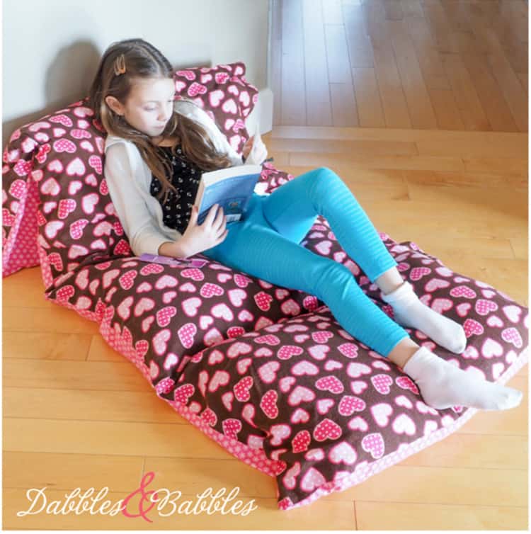 girl reading while seated on a pillowcase bed made from repurposing pillowcases 