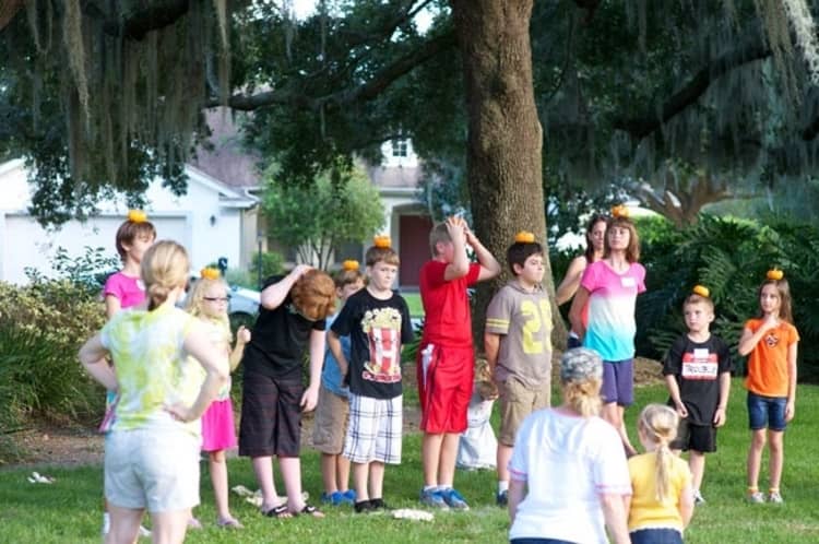 kids balancing mini pumpkins on their heads in readiness for a pumpkin run as part of Halloween games