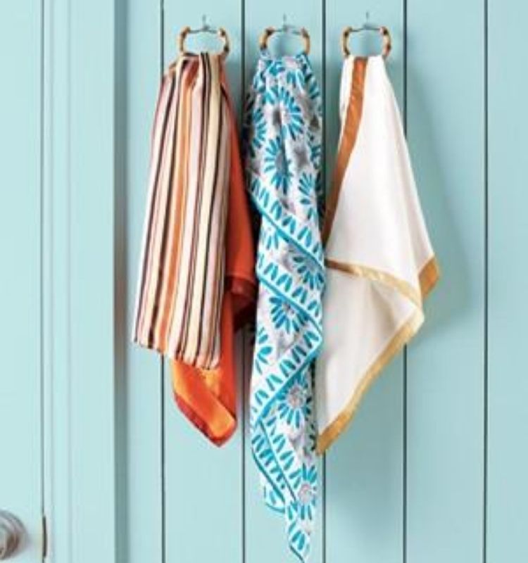 three scarves hanging from shower curtain rings attached to an aqua blue wall