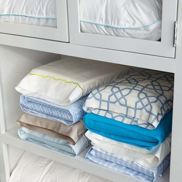 organized linen closet with the bedsheets and extra pillowcase inside one pillowcase