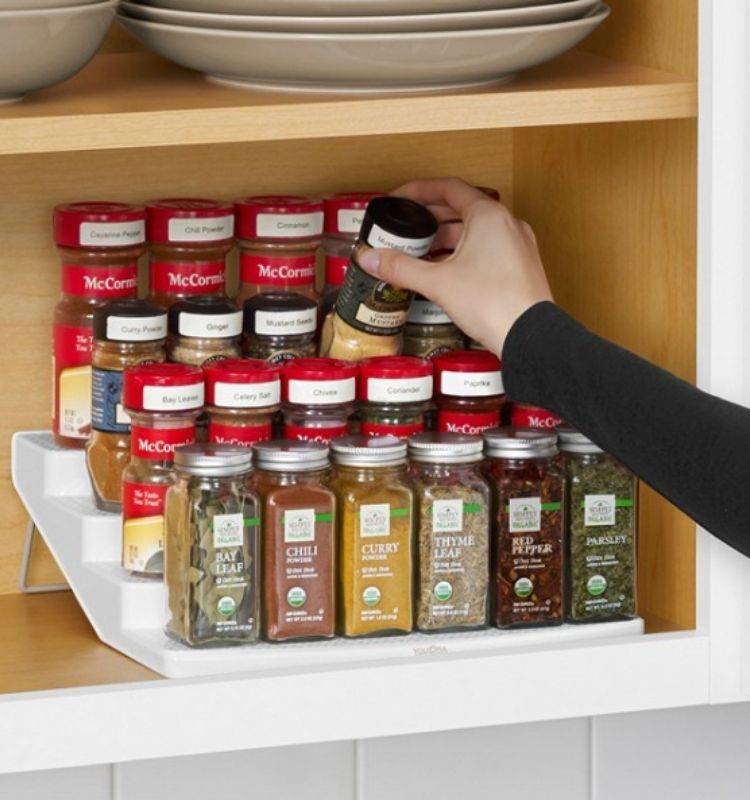 a hand placing a spice jar back on a tiered rack full of other spices