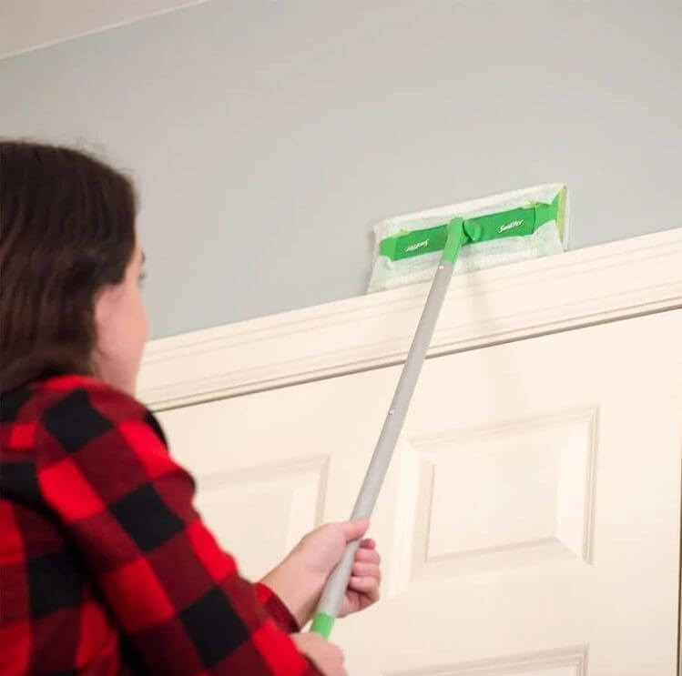 A woman dusting a wall using a Swifter Sweeper with dry cloth on the end