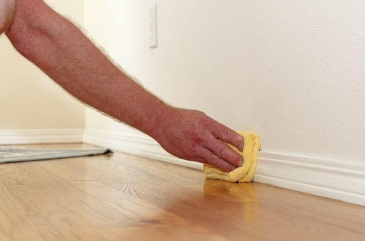 A person cleaning baseboards using a microfiber cloth