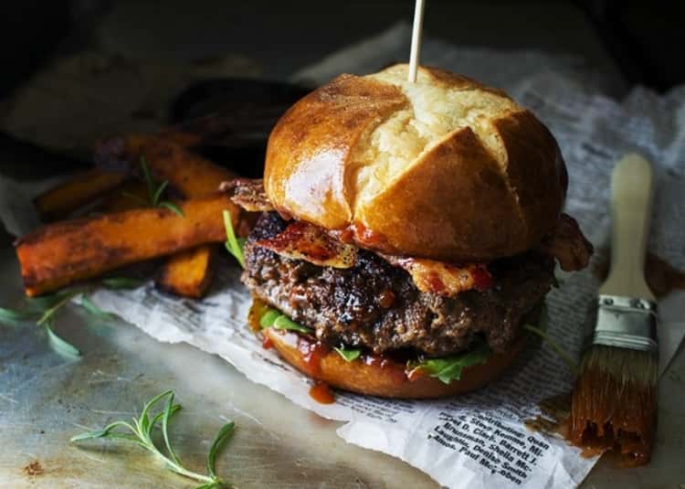 Beef burger on a pretzel bun with lettuce, Dr. Pepper barbecue sauce, and bacon.