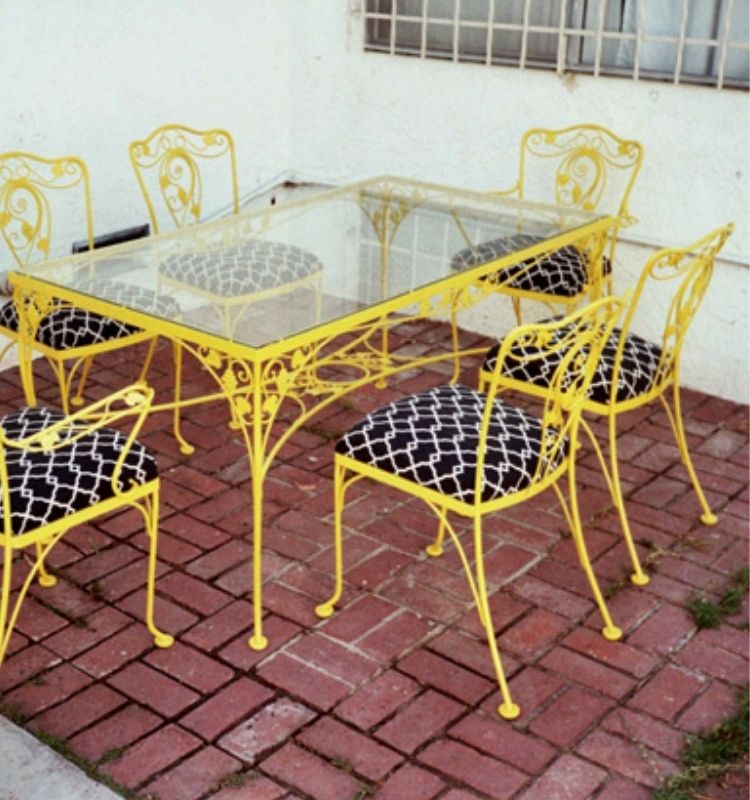 iron outdoor furniture dining table with chairs painted bright yellow with dark fabric cushions