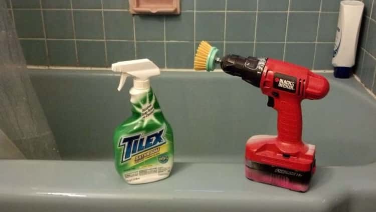 Cordless drill with scrubber attached and a bottle of cleaner sitting on the edge of the bath tub