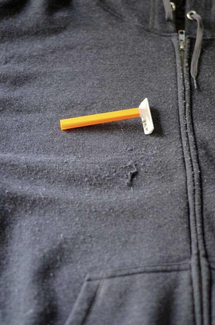 a gray sweat shirt with pulls and a razor with orange handle laying on it remove pills clothing hacks