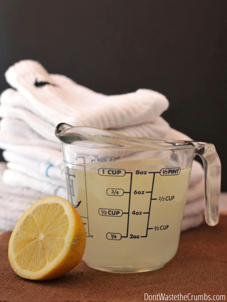 a lemon, a measuring cup with solution and a pile of towels in the background