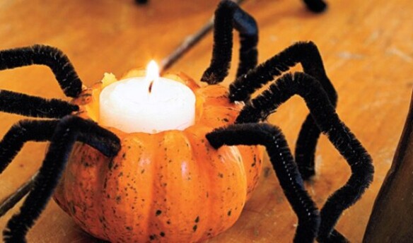 A pumpkin shaped votive candle holder with black pipe cleaner spider legs.